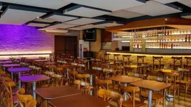 Vista do interior moderno do Vinicius Show com mesas de madeira e bar iluminado